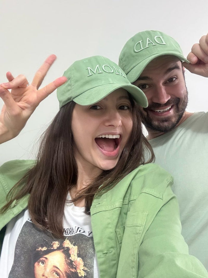 Casal sorrindo com os bonés MOM e DAD da Gestar